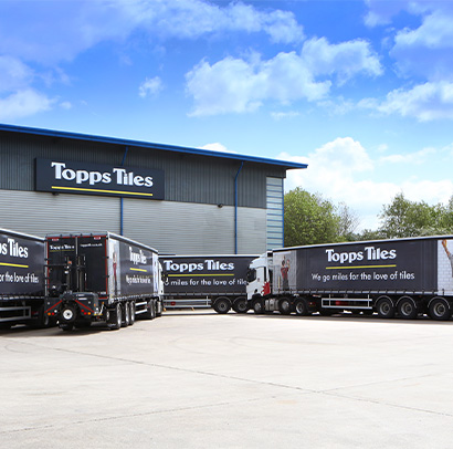 Topps Tiles warehouse with many Topps Tiles delivery trucks parked outside of it. 
